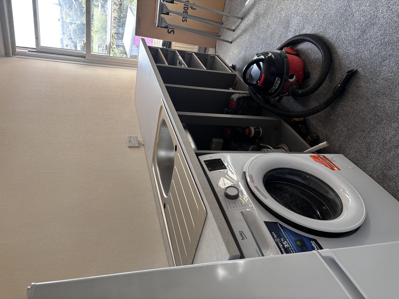 Sink set into worktop, washing machine slid under — plumbing connections being made