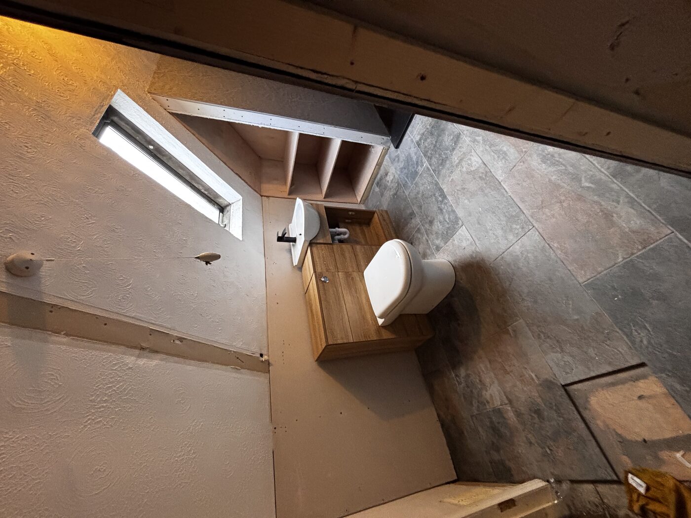 Toilet and oak vanity unit fitted, tiles complete, shower area behind stud wall