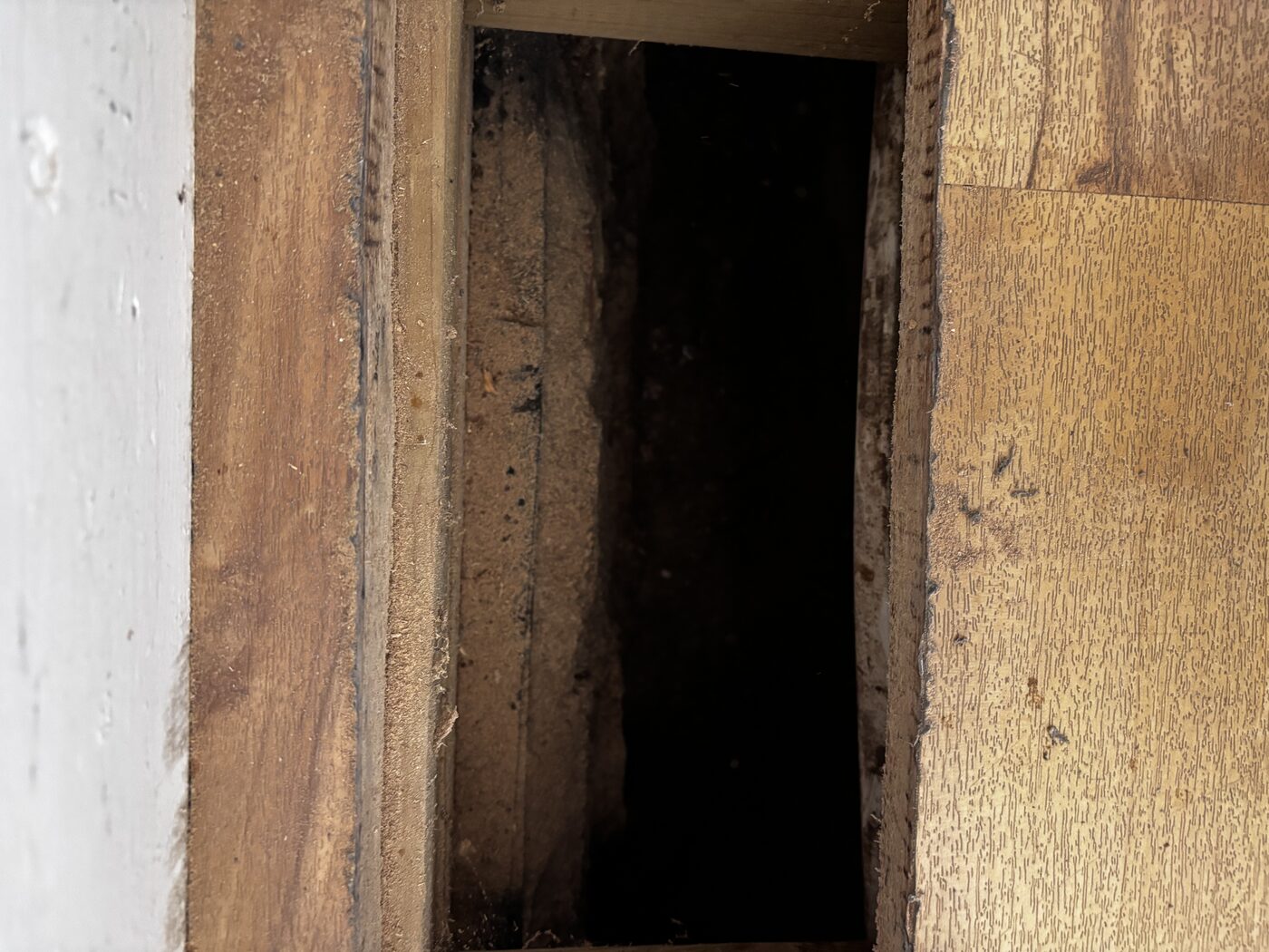 Looking into the floor void — tracing the pipe run beneath the boards