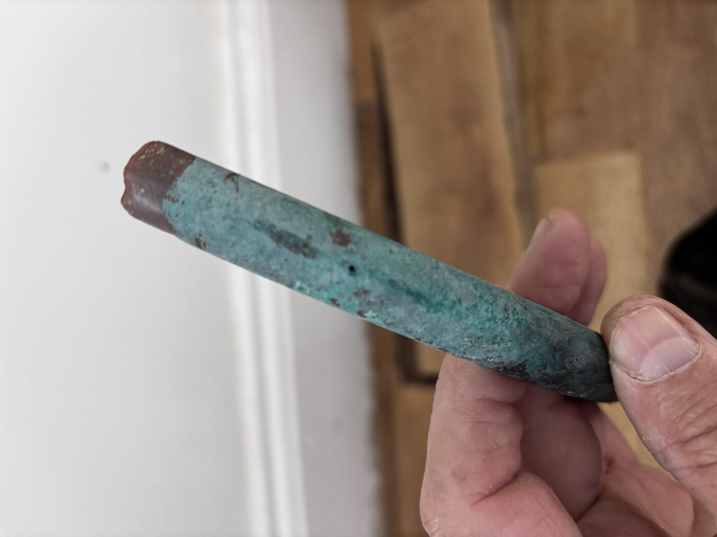 The culprit — heavily corroded copper section with pinhole, green with age