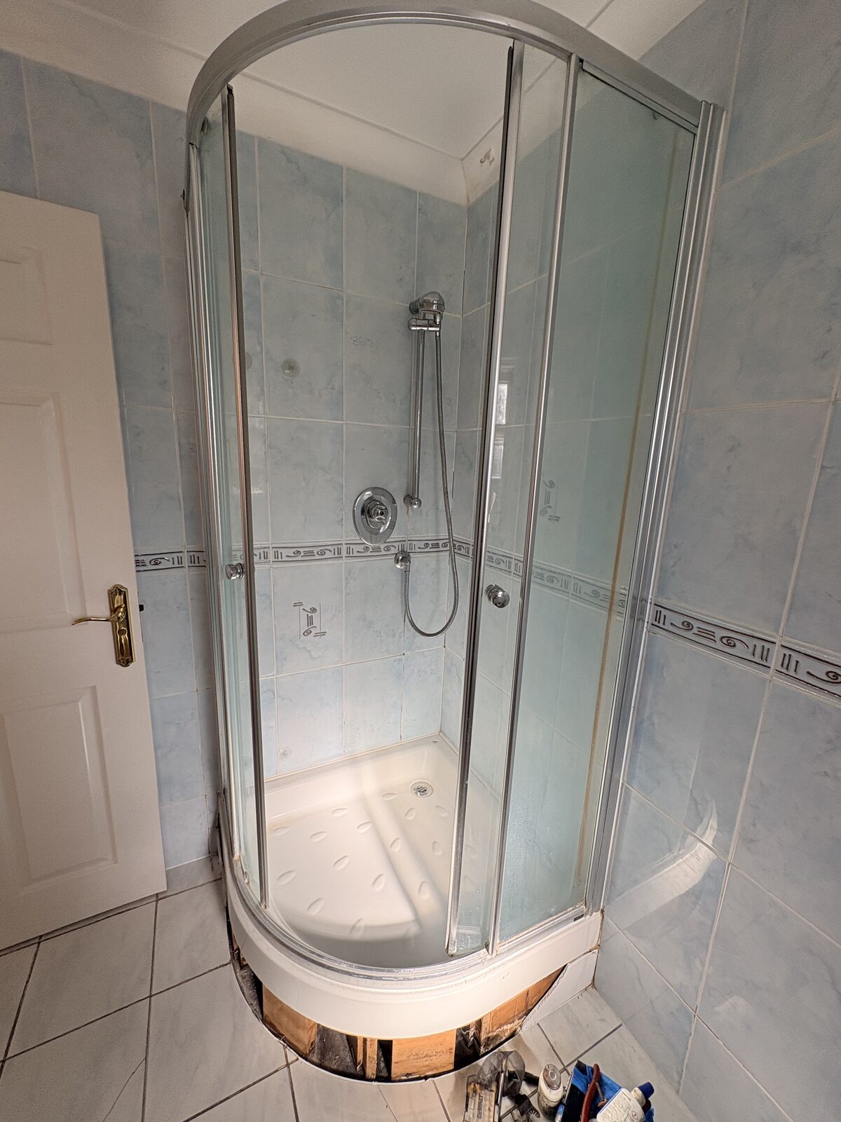Original blue-tiled shower before the wall-panel upgrade, with the existing enclosure
