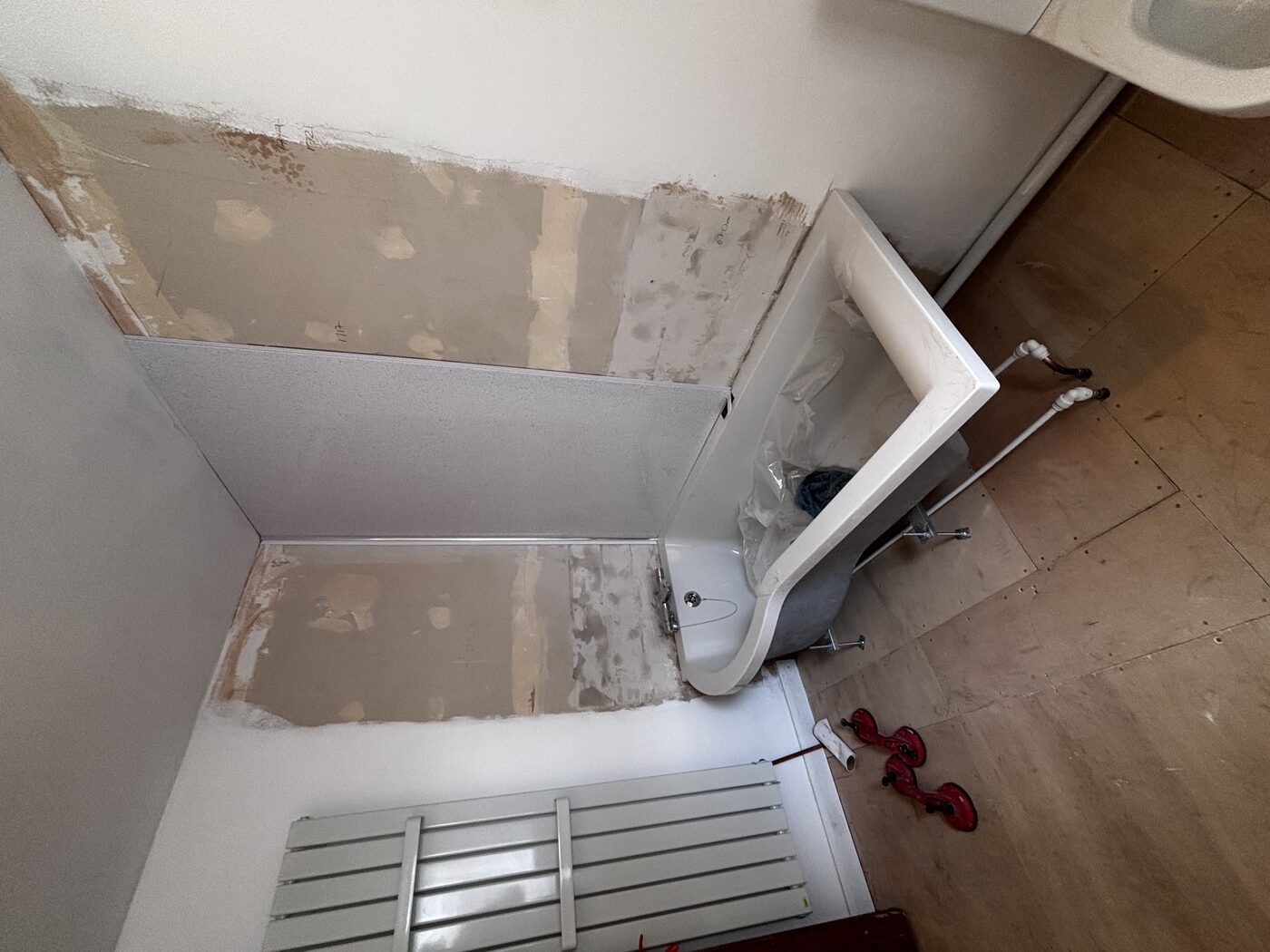P-shaped bath positioned, walls stripped back, first aqua panel being fitted